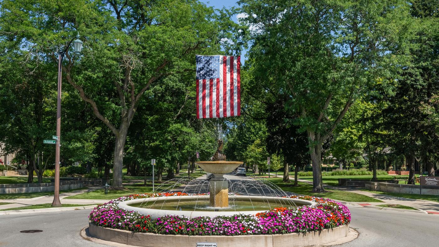 The fountain circle in Kenilworth, planted with flowers, with an American flag hung above it